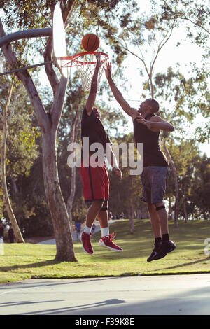 Two young men shooting basketball hoops in the park at sunset Stock Photo