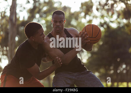 Two young men playing basketball in the park at sunset Stock Photo