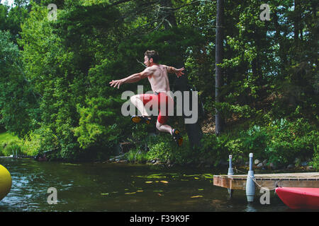 Man jumping off a jetty into a lake Stock Photo