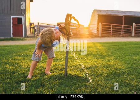 Boy drinking water from tap on a farm Stock Photo