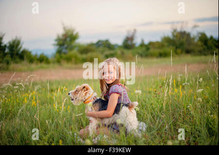 Portrait of a smiling Girl sitting in the countryside hugging her fox terrier dog Stock Photo