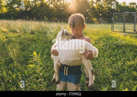 Boy standing in a meadow carrying a young goat
