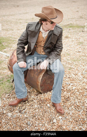 Elevated view, of a modern day cowboy sitting on a rusty oil drum. Stock Photo