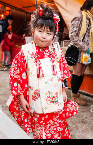 Five year old Japanese girl, slightly over weight with chubby cheeks, standing posing for viewer while wearing red and pink kimono. Cheeky expression. Stock Photo