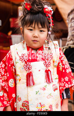 Five year old Japanese girl, slightly over weight with chubby cheeks, standing posing for viewer while wearing red and pink kimono. Cheeky expression. Stock Photo