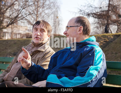 two older men talk on a park bench on sunny autumn day Stock Photo