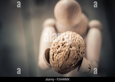 Wooden figure holding walnuts on an old wooden table. Stock Photo