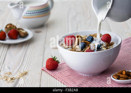 Pouring milk into the bowl with multigrain natural flakes with blueberries and raspberries Stock Photo