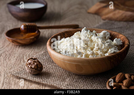 Cottage cheese in a wooden bowl on a textured wooden surface, close up view Stock Photo