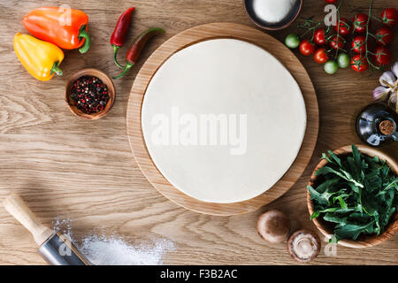 Fresh dough pizza base  and ingredients on a wooden textured table. Top view. Stock Photo