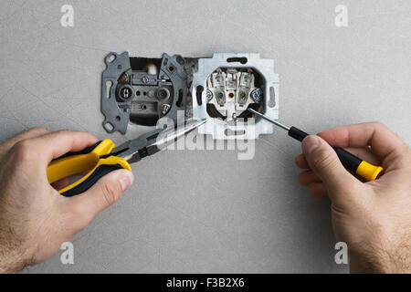 Installing a wall-mounted AC power socket with a screwdriver on a grey wall, renovating home. Close up view. Stock Photo