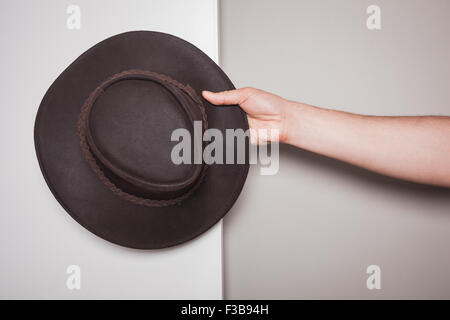 A hand is holding a cowboy hat against a dual colored green and white background Stock Photo