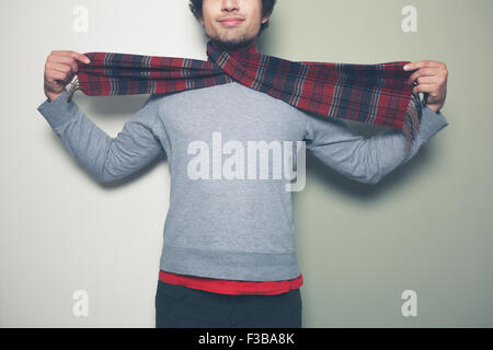 A young man with a scarf around his neck is standing against a split colored green and white background Stock Photo