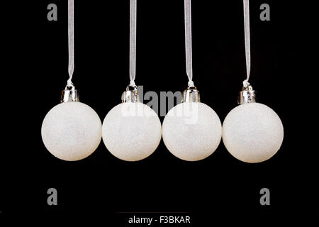 Four white christmas balls hanging in a horizontal row isolated on black background Stock Photo