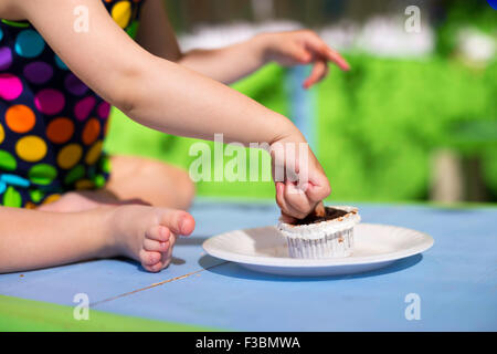 Cute baby wearing spotted swimsuit tasting a cupcake with her finger on a blue table Stock Photo