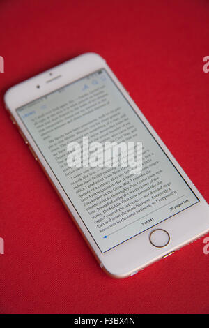 Reading an ebook on a Gold and white Apple iPhone 6 against a red background Stock Photo
