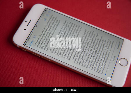 Reading an ebook on a Gold and white Apple iPhone 6 against a red background Stock Photo