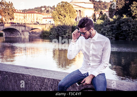 Portrait of contemplative light brown haired young man wearing white shirt beside picturesque river or lake, looking away to a s Stock Photo