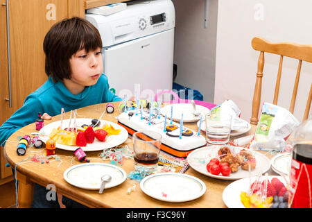 Mixed ethnicity, (Japanese English) 11 year old boy sitting at head of kitchen table blowing candles out on birthday cake. Other foods and drinks. Stock Photo
