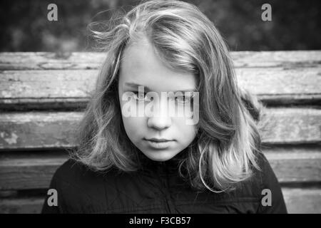 Beautiful Caucasian blond teenage girl in black sitting on old wooden bench in autumn park, monochrome photo Stock Photo