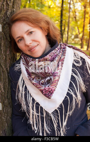 Beautiful Young Caucasian woman in traditional Russian Pavloposadskie neck scarf stands in autumnal park Stock Photo