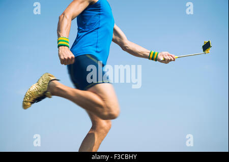 Modern athlete in gold shoes running with his smartphone on the end of a selfie stick Stock Photo