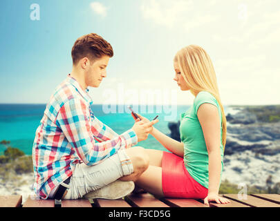 couple with smartphones sitting on bench Stock Photo
