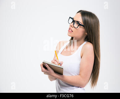 Portrait of a cute female student making notes in notepad and looking away isolated on a white background Stock Photo