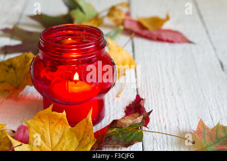 Red lantern candle with autumn leaves on white boards closeup Stock Photo