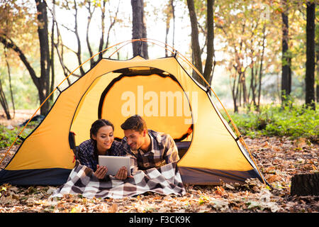 Portrait of a smiling couple lying in tent and using tablet computer in forest Stock Photo
