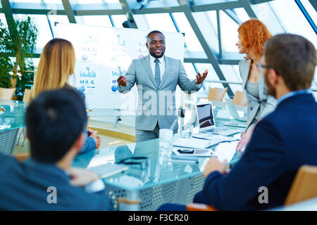 African-american businessman standing by whiteboard and voicing his opinion about data analysis to colleagues Stock Photo
