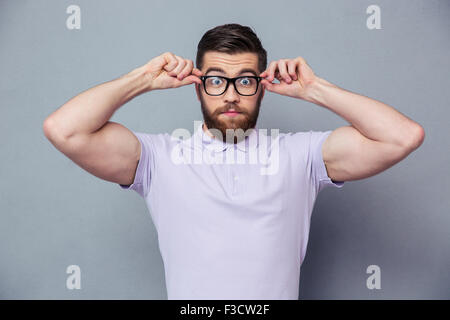 Portrait of amazed casual man looking at camera through glasses over gray background Stock Photo