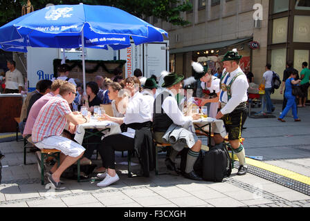 Munich, Germany -July 07: People having bear sitting in the street. Some dressed in traditional Bavarian dress clothes some with Stock Photo