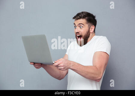 Portrait of a cheerful man using laptop computer over gray background Stock Photo