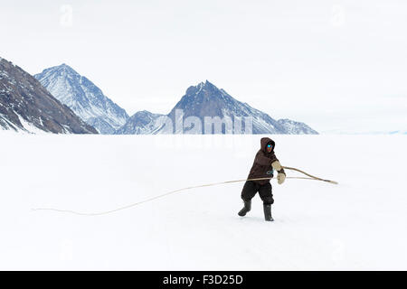 Inuit young boy practicing with traditional dog whip on the floe edge, Baffin bay, Nunavut, Canada. Stock Photo