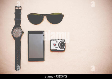 Wristwatch, sunglasses, smart phone and very small action camera layed down on floor. Male accessories. Stock Photo