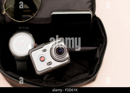 Wristwatch, sunglasses, smart phone and very small action camera in little black men bag. Male accessories. Stock Photo