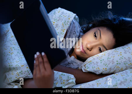 Young woman lying in bed, using digital tablet