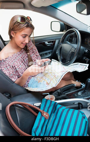 Woman checking phone in car with map on lap Stock Photo