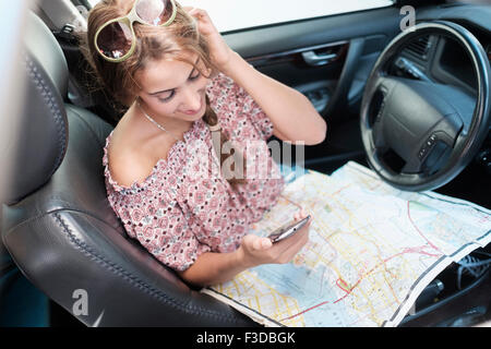 Woman checking phone in car with map on lap Stock Photo