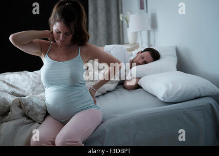 Woman sitting on bed and stretching stiff neck Stock Photo