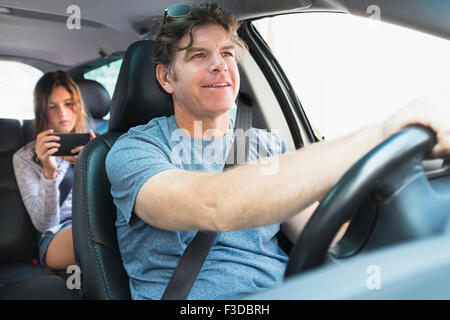 Man driving car, girl (10-11) texting in background Stock Photo