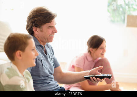 Children (8-9, 10-11) watching TV with their father Stock Photo