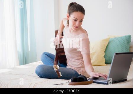 Woman with laptop and guitar on bed Stock Photo