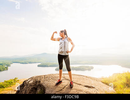 Young woman standing on top of mountain and flexing muscles Stock Photo