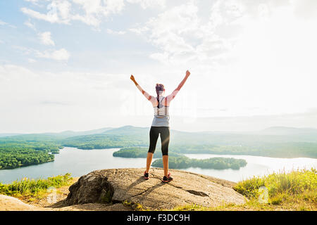 Young woman standing on top of mountain with outstretched arms, rear view Stock Photo