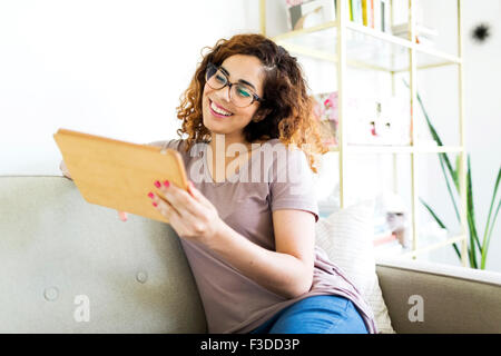 Woman sitting on sofa, using digital tablet Stock Photo