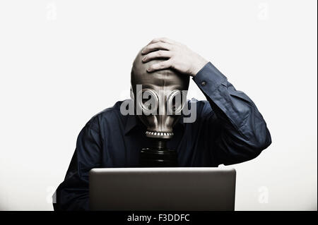 Studio shot of man in front of laptop wearing gas mask Stock Photo