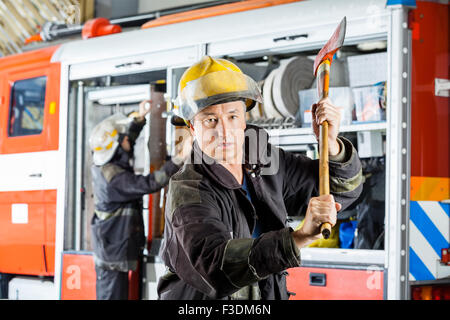 Confident Fireman Holding Axe At Fire Station Stock Photo