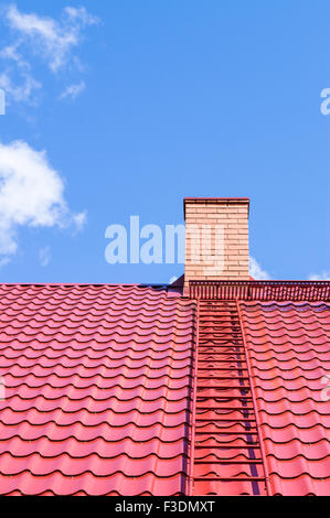 Brick chimney on red roof with metal ladder against blue sky Stock Photo